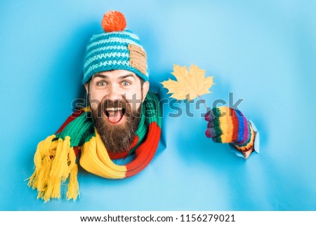 Happy bearded man with autumnal maple yellow leaf in hand. Bearded man in colorful hat look through paper and hold autumn leaf. Autumn mood. Autumn time. Isolated. Through paper. Emotions.