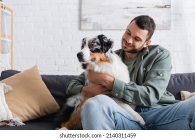 happy bearded man cuddling australian shepherd dog on sofa - Powered by Shutterstock