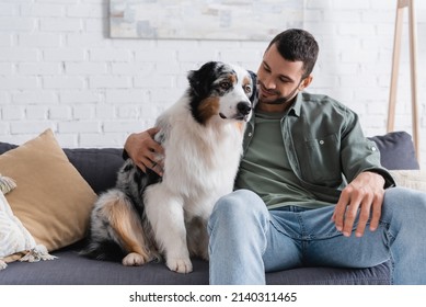 Happy Bearded Man Cuddling Australian Shepherd Dog On Couch