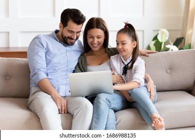 Happy Bearded Man Embracing Smiling Wife And Adorable School Aged Girl, Watching Funny Video On Computer. Affectionate Family Of Three Playing Game On Laptop Or Shopping Online In Internet Store.