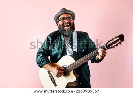 Happy bearded man playing acoustic guitar on pink background.