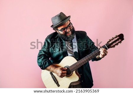 Happy bearded man playing acoustic guitar on pink background.