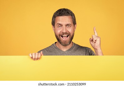 happy bearded man raised finger inspired with idea behind yellow paper for copy space, advertisement