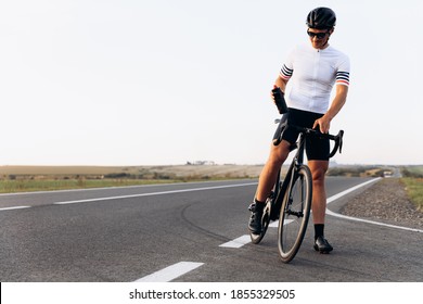 Happy Bearded Man In Sport Outfit, Helmet And Glasses Standing Outdoors With Black Bike. Smiling Guy Cycling On Paved Road During Sunny Day.