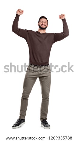 A happy bearded man stands in casual wear smiling and holding arms up in victory in tight fists. Victory and success. Receiving praise. Reaching goals.