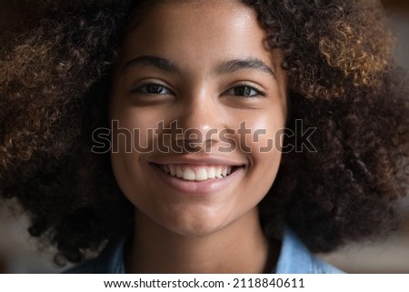 Happy beautiful African American teenage girl with Afro hairstyle looking at camera with toothy smile. Close up face portrait. Black teen high school student, schoolgirl head shot portrait