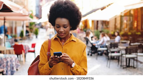Happy beautiful african american woman texting on mobile phone while walking outdoors. Portrait of young african american female typing on smartphone on street in city.  - Shutterstock ID 1820849336