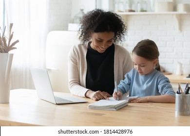 Happy beautiful african ethnicity woman tutor giving private educational lesson to focused small kid girl. Smiling mixed race mother helping little adopted child daughter with school homework.