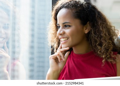 Happy beautiful african woman standing by a window in modern office looking outside and smile with her hand on her chin. Productive job concept at comfy place. - Shutterstock ID 2152984341