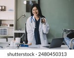 Happy beautiful asian female pharmacist wearing lab coat standing and holding pill bottle, She looking at camera feels good, trustworthy and proud of his work in the pharmacy drugstore.