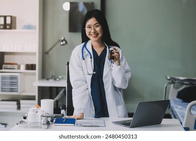 Happy beautiful asian female pharmacist wearing lab coat standing and holding pill bottle, She looking at camera feels good, trustworthy and proud of his work in the pharmacy drugstore. - Powered by Shutterstock