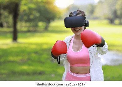 Happy and beautiful asian fitness fashion female sportswoman with VR virtual reality headset boxing game technology morning working out aerobic training for boxing punch under the tree in the park - Powered by Shutterstock