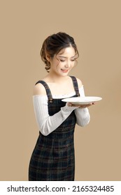 Happy Beautiful Asian Model Holding A Plate With Copy Space For Separate Products On Beige Background.