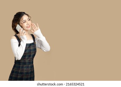 Happy Beautiful Asian Model Holding Mobile Phone With Copy Space For Separate Products On Beige Background.