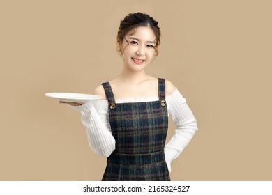 Happy Beautiful Asian Model Holding A Plate With Copy Space For Separate Products On Beige Background.