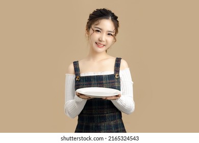 Happy Beautiful Asian Model Holding A Plate With Copy Space For Separate Products On Beige Background.