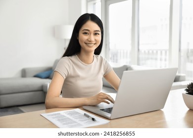 Happy beautiful Asian student girl studying at laptop at home, using elearning platform for online education, sitting at table with computer, looking at camera, typing, smiling - Powered by Shutterstock