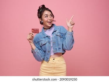 Happy beautiful Asian teen shopaholic women showing credit card and her finger pointing isolated on pink background.