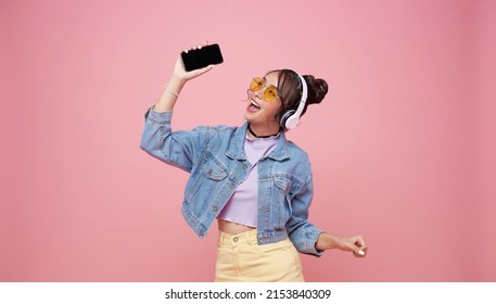 Happy Beautiful Asian Teen Woman In Yellow Glasses Listening Music In Headphones And Dance On Pink Background.