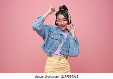 Happy Beautiful Asian Teen Woman In Yellow Glasses Listening Music In Headphones And Dance On Pink Background.