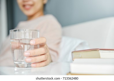 Happy Beautiful Asian Woman Drink Water During Wake Up On Morning At The Bedroom. Smiling Girl Holding Transparent Glass On Bed. Healthy Food.