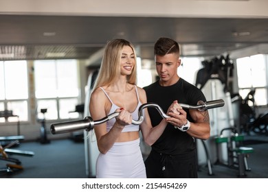 Happy beautiful athletic woman with a smile and a slender body working out in the gym with a fitness instructor. Handsome bodybuilder trainer man trains and helps a beautiful girl