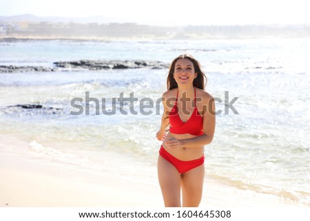 Happy beautiful bikini girl coming out of water walking enjoying on tropical beach. Carefree young woman with slim weight loss body sunbathing in summer vacation travel.