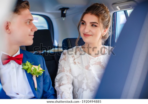 Happy\
beautiful bride and groom sitting in the trunk of the car. Groom\
with red bow tie. Honeymoon, fun and\
laughter.