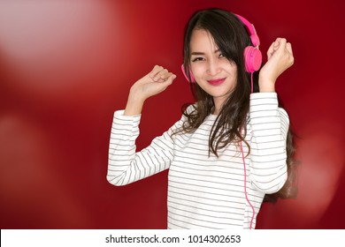 Happy Beautiful Brunette Asian Girl Listening Music In Headphones And Dancing On Red Background