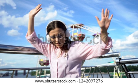 Happy beautiful brunette dancing in headphones on pier, successful and confident