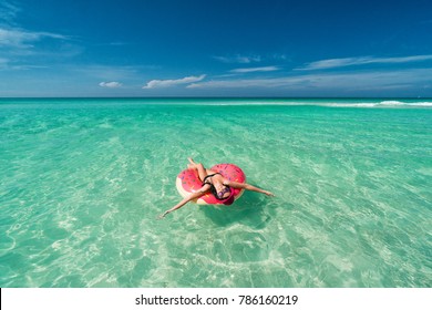 Happy beautiful brunette woman in pink hat swims on big inflatable tube at the coast of Caribbean Sea in summer sunny day
