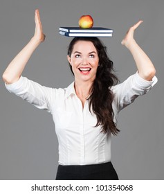 A happy beautiful business woman balancing books and an apple on her head