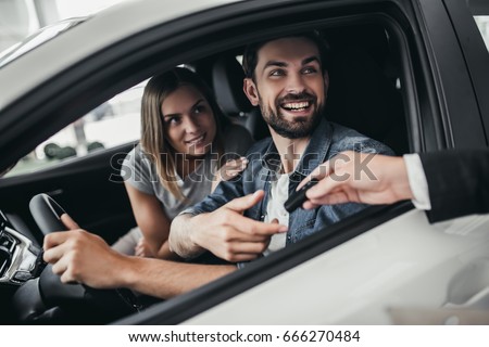Happy beautiful couple is choosing a new car at dealership.