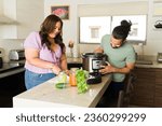 Happy beautiful couple laughing and having fun while preparing lunch or dinner in the pressure cooker doing house chores in the kitchen