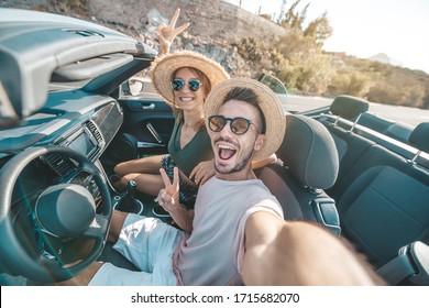 Happy beautiful couple in love taking a selfie portrait driving a convertible car on the road at vacation. Rental cars, holidays and people. - Powered by Shutterstock