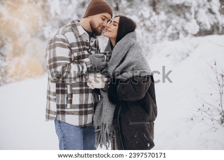 Happy beautiful couple resting and drinking hot tea in the forest in winter in the mountains