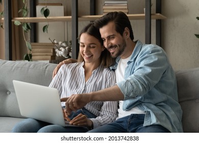 Happy beautiful couple sit on sofa enjoy easy purchasing on-line using laptop. Booking hotels, planning vacation, choose goods fashion items on internet for modern house. E-commerce services concept
