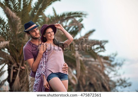 Happy beautiful couple spends rest outside. Travelers walking in the tropical park. Active rest. Palm-trees on background.