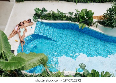 Happy beautiful couple sunbathing by swimming pool of spa hotel with fruit cocktails, view from above - Powered by Shutterstock