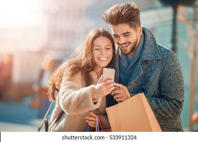 Happy Beautiful Couple Using Smart Phone And Shopping Together.