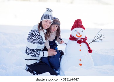 Happy Beautiful Family Building Snowman In Garden, Winter Time, Mom And Kid