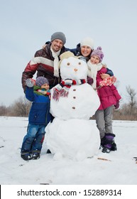 Happy Beautiful Family With Two Kids Building Snowman Outside In Winter Time