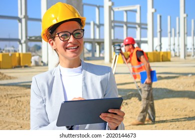 Happy beautiful female architect with tablet on construction site. She is smiling and satisfied with her job, behind her construction engineer with measuring device, positive emotions