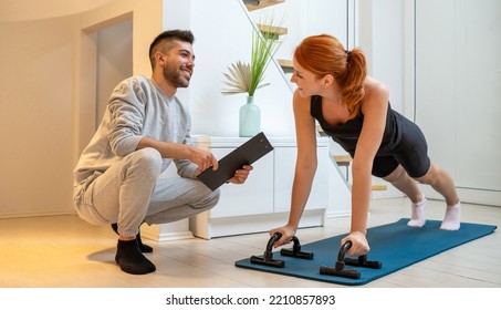 Happy beautiful ginger woman doing home workout, push up exercise with assistance of her personal trainer at home in living room. - Powered by Shutterstock