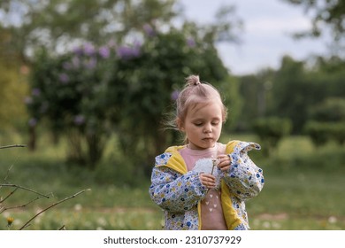 Happy beautiful girl of 3 years blowing on a dandelion on a sunny summer evening. A child in the fresh air, in nature. The setting sun. - Shutterstock ID 2310737929