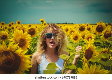 Happy beautiful girl among the sunflowers field on sunglasses in summer 