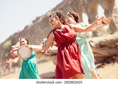 Happy beautiful girl dancing with another girls dressed in ancient roman greek historic style celebrating a pagan solstice and equinox rite and ritual with isntruments in an open field