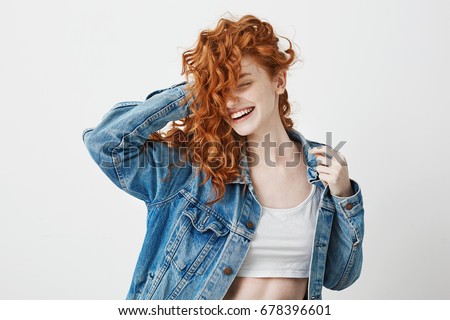 Happy beautiful girl smiling with closed eyes touching her red curly hair over white background.