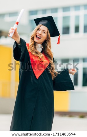 Happy beautiful girl student, in a master's dress, holding a diploma from the University. Concept of the graduation ceremony