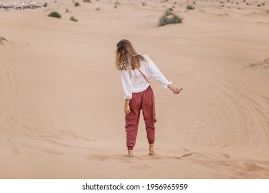 Happy beautiful girl in trousers harem pants standing in the middle of the desert. Safari excursion. Dunes and sand. 
